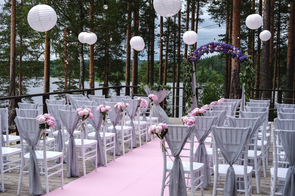 Wedding arch and grey chairs with peonies standing in ceremony area in woods.